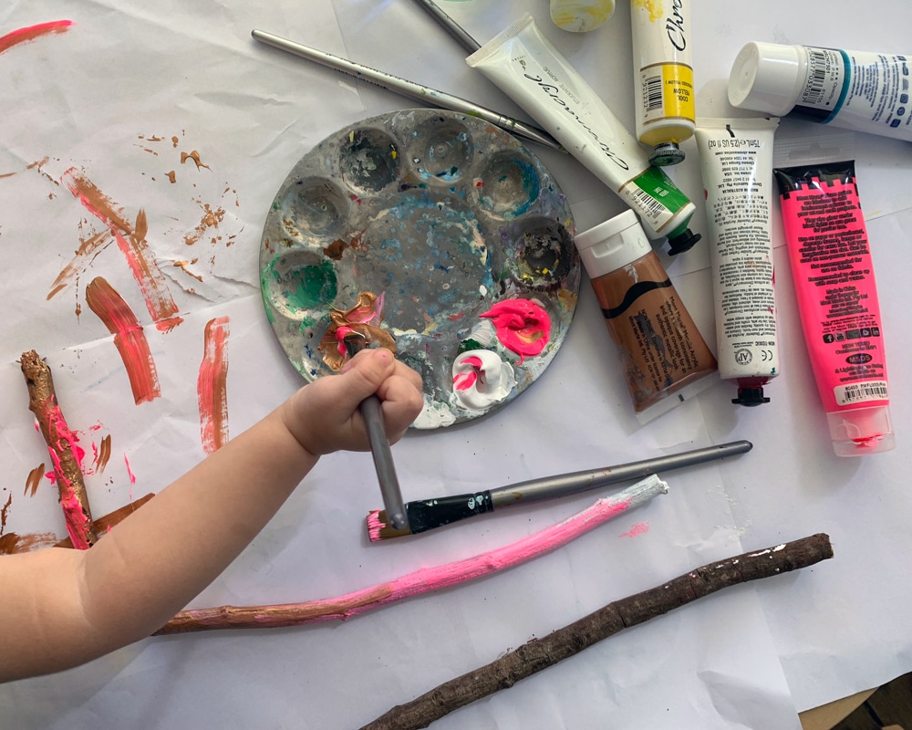 Bird's eye view of child holding paint brush and painting sticks