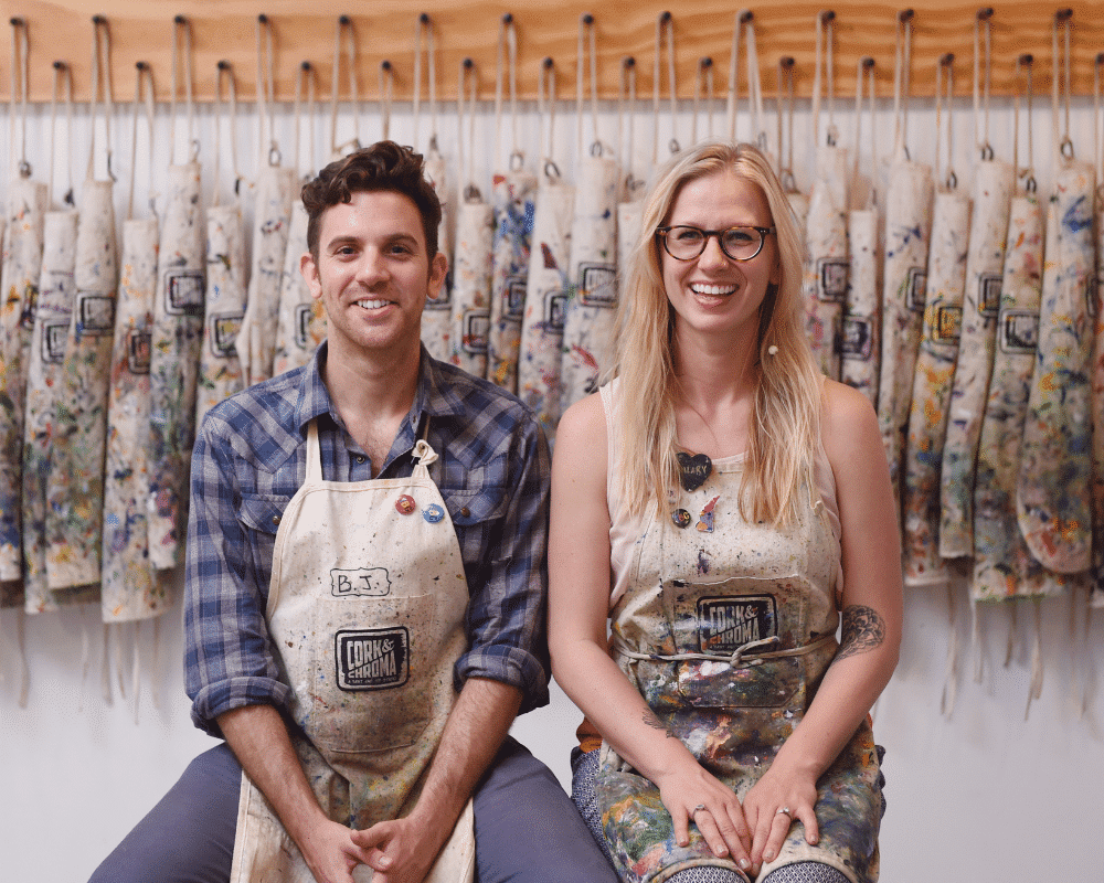 Hillary & B.J. sitting in front of Cork & Chroma aprons
