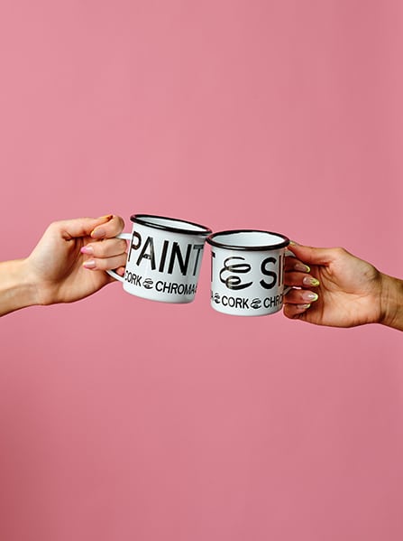 Two Paint & Sip Enamel Mugs by Cork & Chroma, clinking.