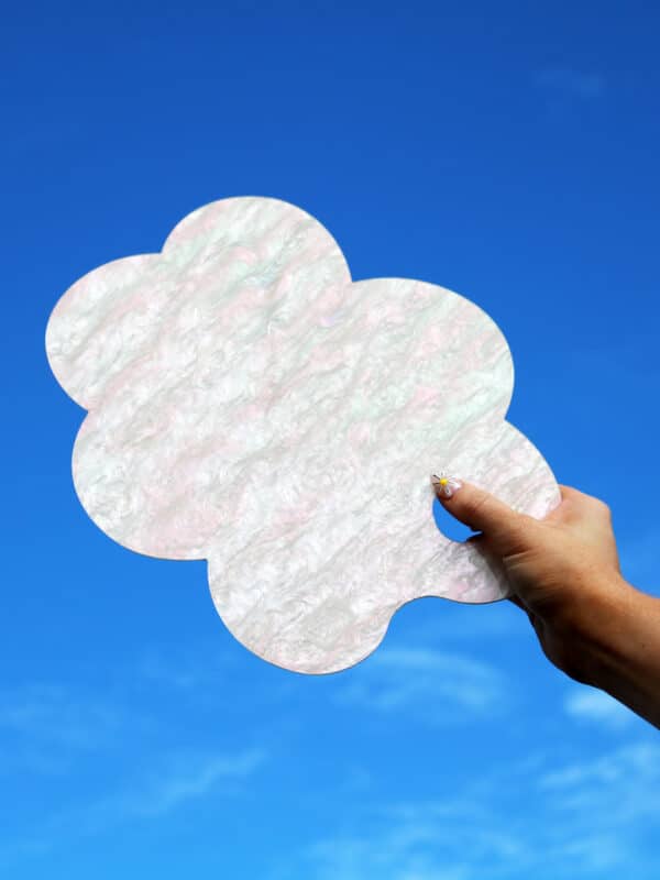 A hand holding Cork & Chroma's Limited Edition acrylic Cloud Palette in Cumulus (cream sparkle) up to the sky