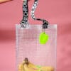 Hand holding a bunch of bananas in the PVC&C Tote Bag by Cork & Chroma with neon green keychain