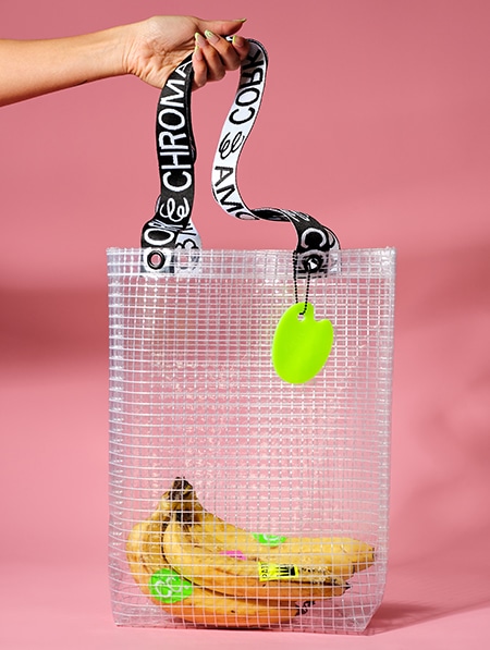 Hand holding a bunch of bananas in the PVC&C Tote Bag by Cork & Chroma with neon green keychain