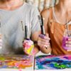 PAINT the Book authors, Hillary Wall and Erin Corstiaans with painting supplies, covered in paint.